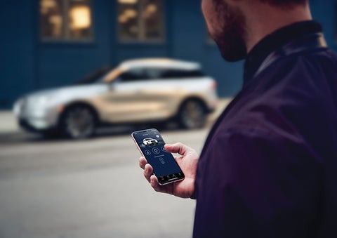 A person is shown interacting with a smartphone to connect to a Lincoln vehicle across the street. | Angela Krause Lincoln of Alpharetta in Alpharetta GA