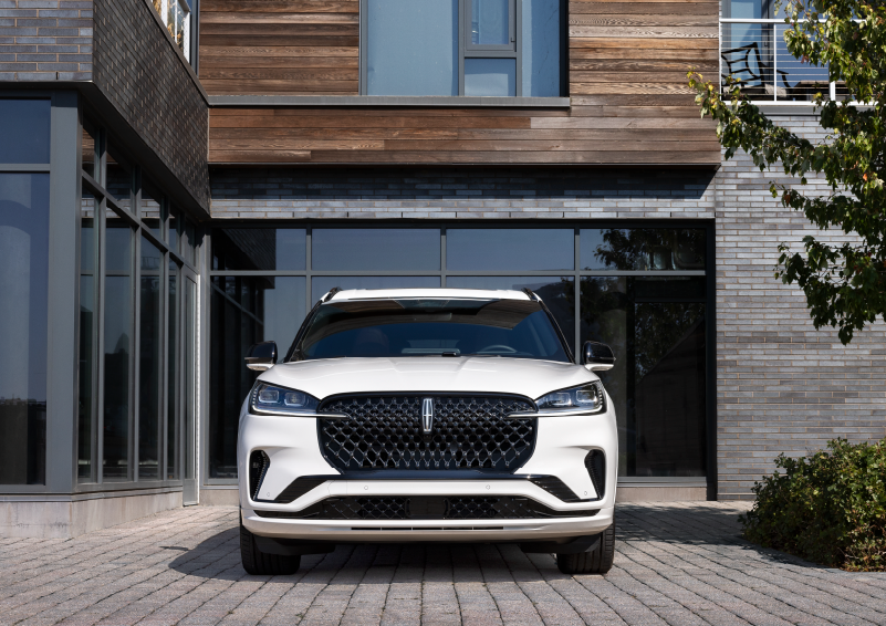 A white 2025 Lincoln Aviator® SUV is shown parked outside a modern building with gray brick and wood accents. | Angela Krause Lincoln of Alpharetta in Alpharetta GA