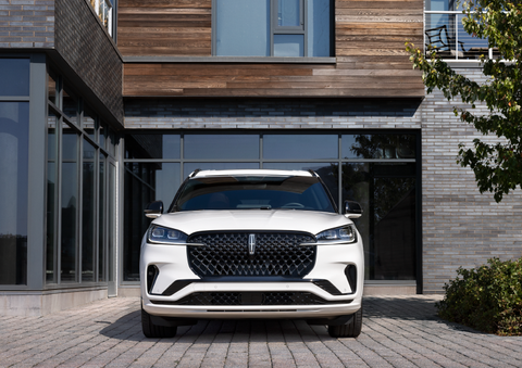 A white 2025 Lincoln Aviator® SUV is shown parked outside a modern building with gray brick and wood accents. | Angela Krause Lincoln of Alpharetta in Alpharetta GA