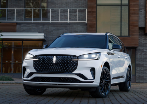 A white 2025 Lincoln Aviator® SUV is shown parked outside a modern building with gray brick and wood accents. | Angela Krause Lincoln of Alpharetta in Alpharetta GA