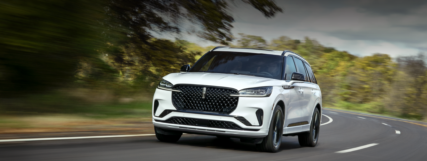 A white 2025 Lincoln Aviator® SUV is being driven down a road lined with trees. | Angela Krause Lincoln of Alpharetta in Alpharetta GA