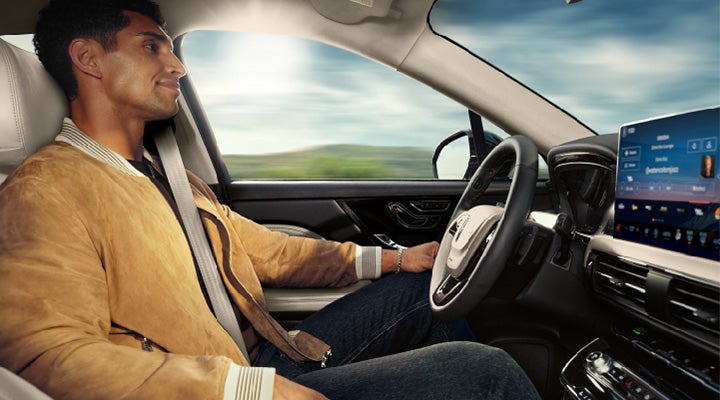A man is seen sitting in the driver's seat of his new Lincoln Corsair® Grand Touring Plug-in Hybrid SUV with his hands off the steering wheel as Lincoln BlueCruise drives his vehicle down a controlled-access highway.