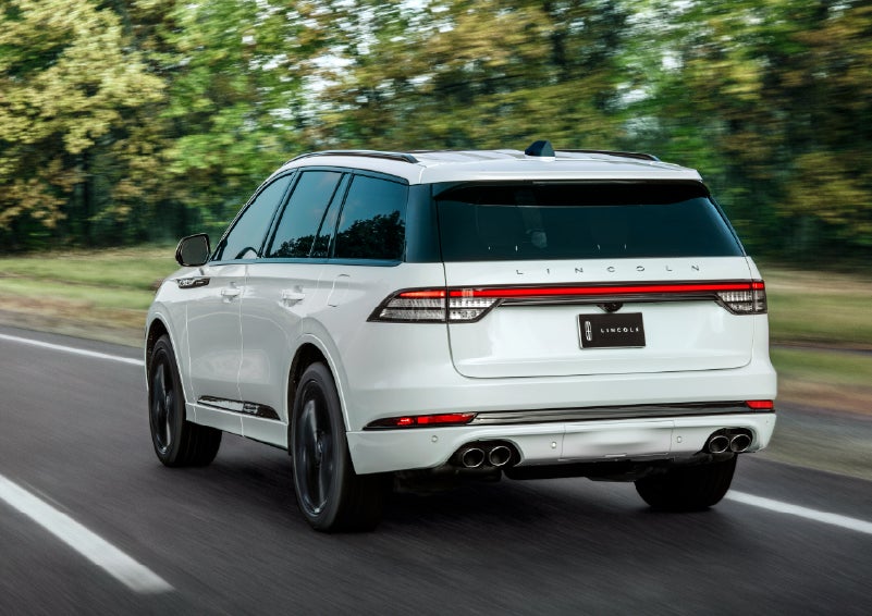 A white 2026 Lincoln Aviator® SUV is being driven away down a road lined with colorful trees. | Angela Krause Lincoln of Alpharetta in Alpharetta GA