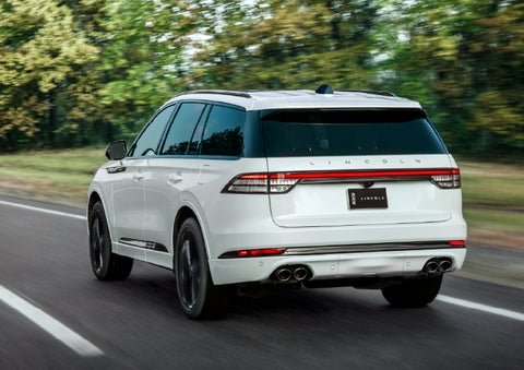 A white 2026 Lincoln Aviator® SUV is being driven away down a road lined with colorful trees. | Angela Krause Lincoln of Alpharetta in Alpharetta GA