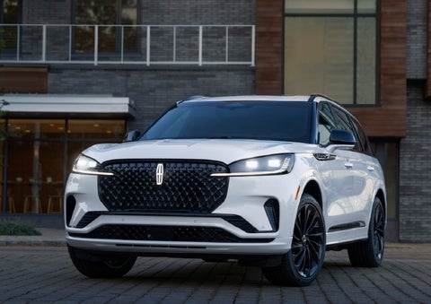 A 2026 Lincoln Aviator® Reserve model is shown with the available Jet Appearance Package parked near a restaurant. | Angela Krause Lincoln of Alpharetta in Alpharetta GA