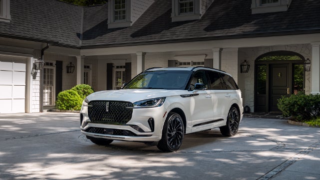 A white 2026 Lincoln Aviator® SUV is parked in the driveway of a luxury home. | Angela Krause Lincoln of Alpharetta in Alpharetta GA